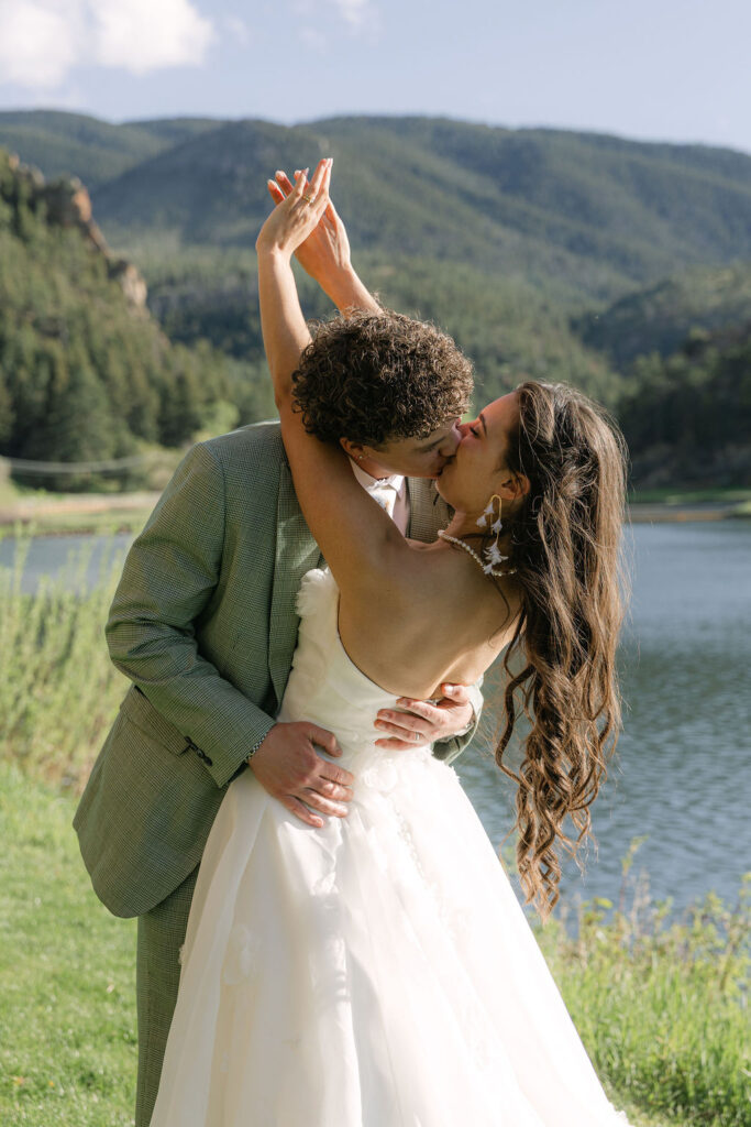 Bride and groom celebrating with arms raised and kissing by mountain lake at Larkspur Colorado wedding with Rocky Mountain backdrop