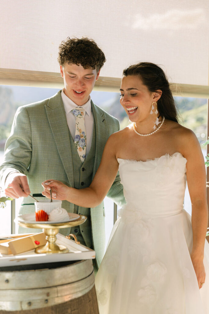 Newlyweds cutting wedding cake together on covered patio with lake views at historic Colorado venue