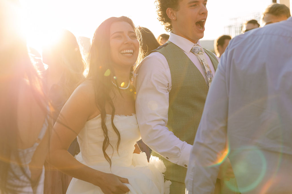 Joyful bride and groom laughing during golden hour at Colorado lakefront wedding with warm sunset lighting and mountain views