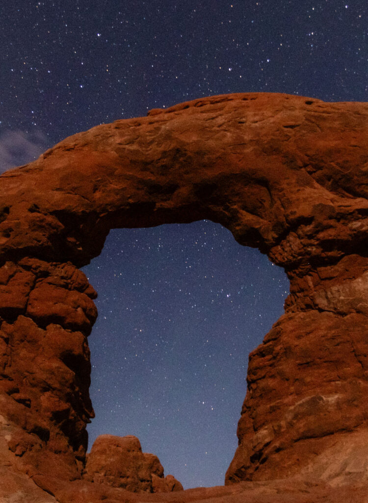 Night sky filled with stars framed by a red rock arch in Arches National Park, capturing the surreal beauty of Moab wedding locations for stargazing elopements and late-night portraits.