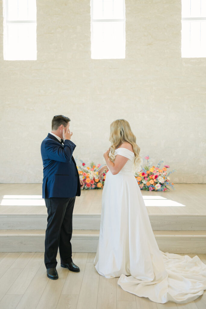 The groom wipes away tears during the first look with his bride inside the chapel at Camp Hosea, a sweet and emotional moment captured by a Texas wedding photographer.