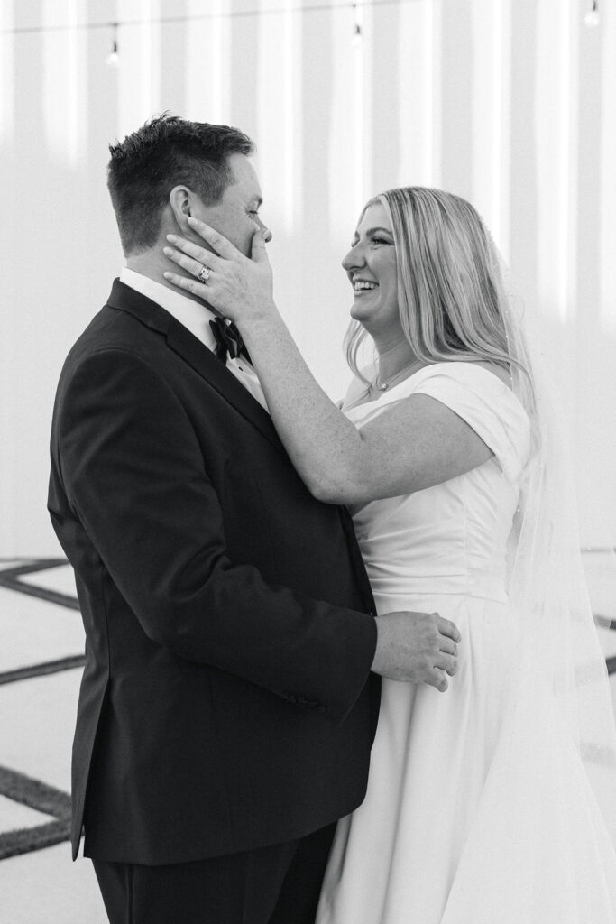 A black-and-white photo of the groom smiling at his bride, capturing a timeless moment inside the Camp Hosea ceremony chapel.