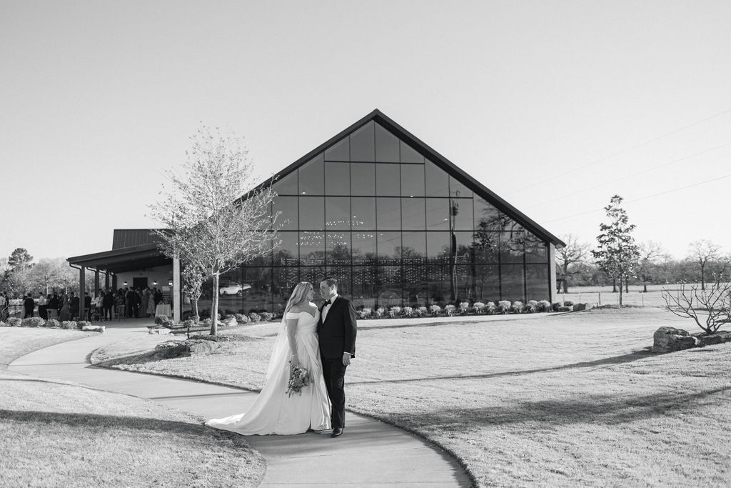 A black-and-white portrait of the bride and groom outside the glass-walled reception space at Camp Hosea, one of the most modern wedding venues in College Station, Texas.