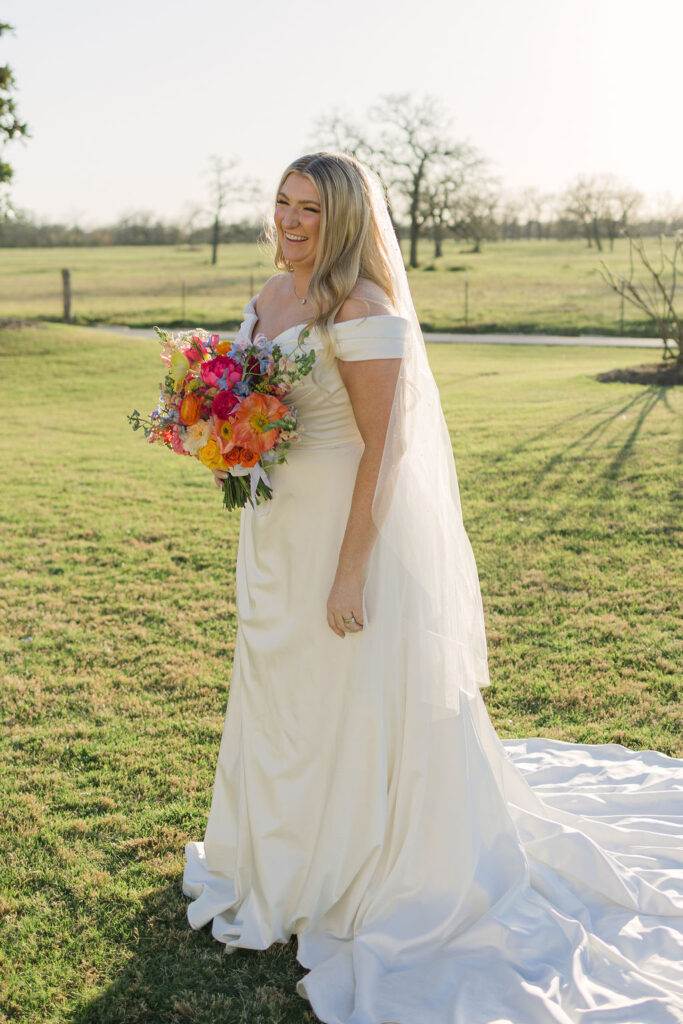 A solo portrait of the bride walking across the courtyard lawn holding her train and smiling with joy at her spring wedding in Texas.
