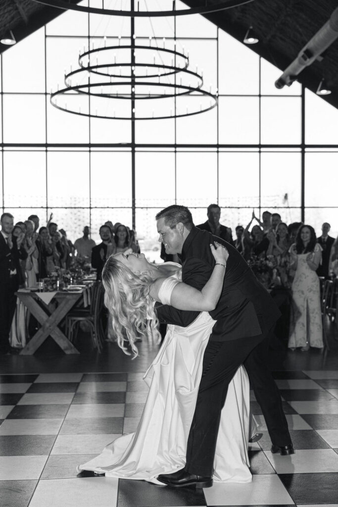 A black-and-white image of the couple’s dramatic dance dip inside the Camp Hosea reception hall, full of joy and movement.