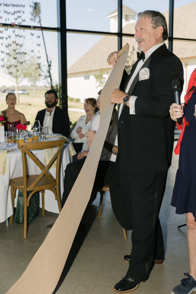 The bride's dad holds up an extra-long toast scroll during the reception, adding a humorous and personal moment to the celebration.