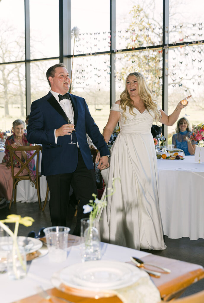 The couple is toasted during their reception, celebrating with loved ones under the glow of the glass-walled venue.