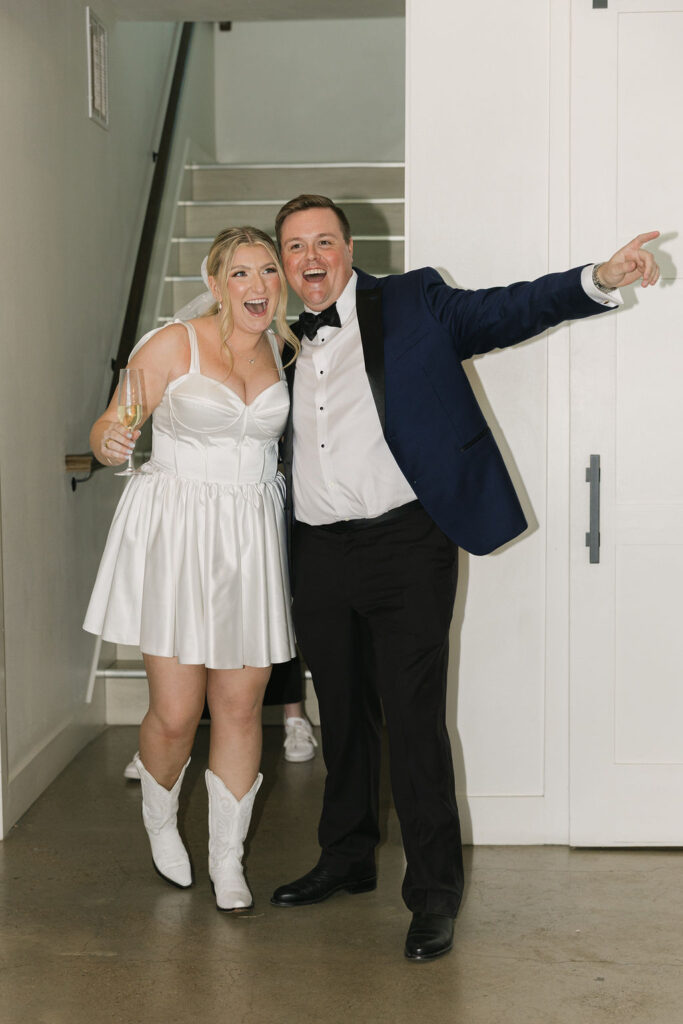 The bride and groom joyfully enter the reception space arm in arm, her short dress and cowgirl boots setting a fun and festive tone.