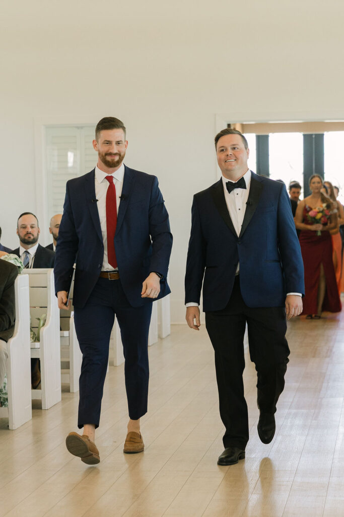 The groom and an officiant walk down the aisle together before the wedding ceremony begins at Camp Hosea, a modern wedding venue in College Station, Texas.