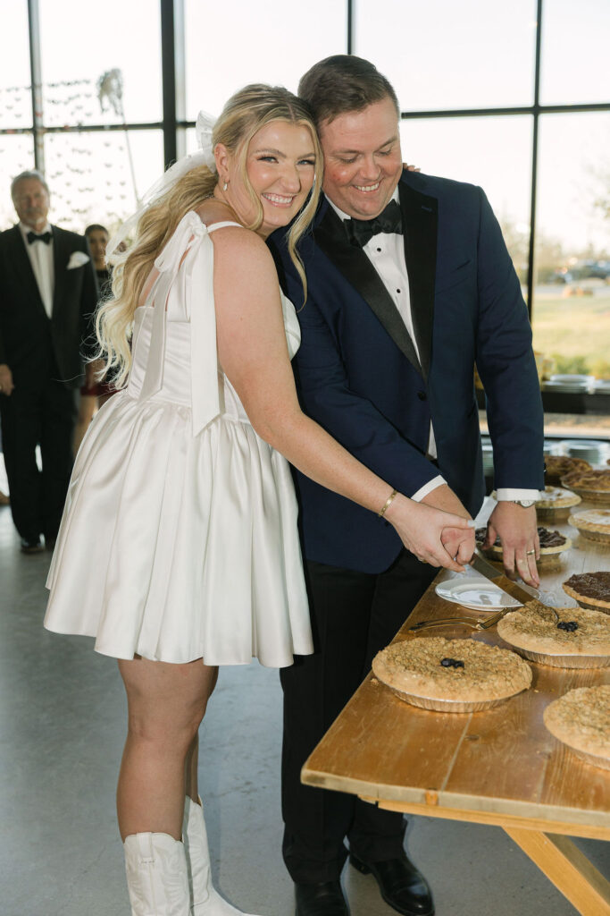 The couple cuts into a table full of homemade pies instead of a traditional cake, adding a cozy and intentional touch to this Camp Hosea wedding.