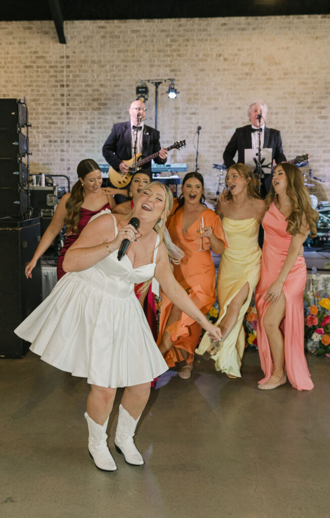 The bride and her bridesmaids sing and dance along with the live band, all in colorful mismatched gowns.