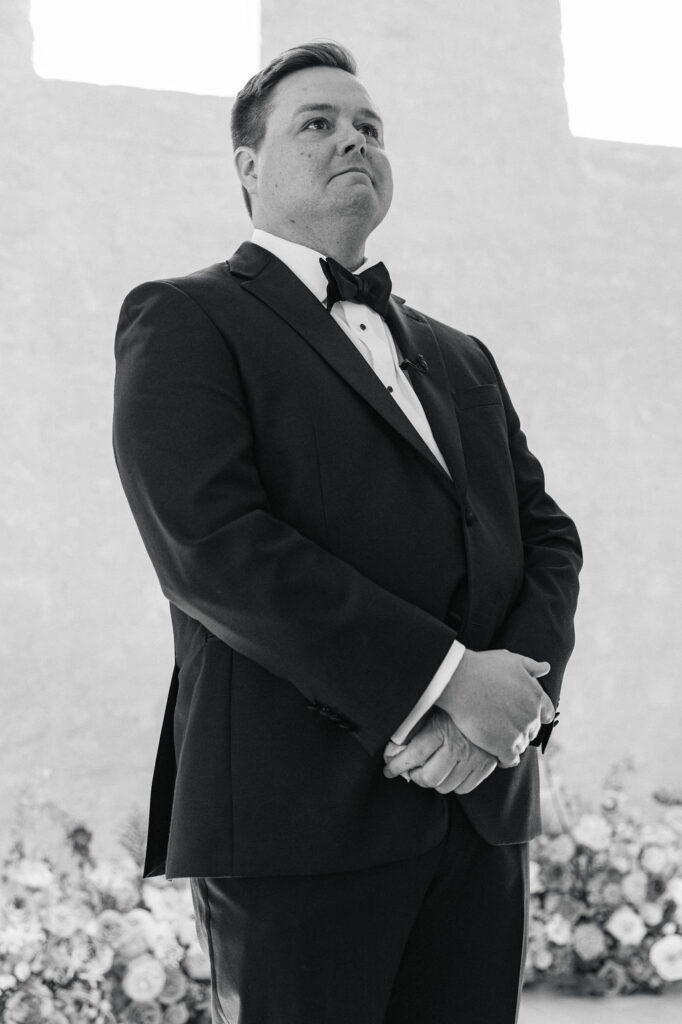 A black-and-white portrait of the groom standing at the altar, emotional and waiting for his bride during this Texas wedding ceremony.