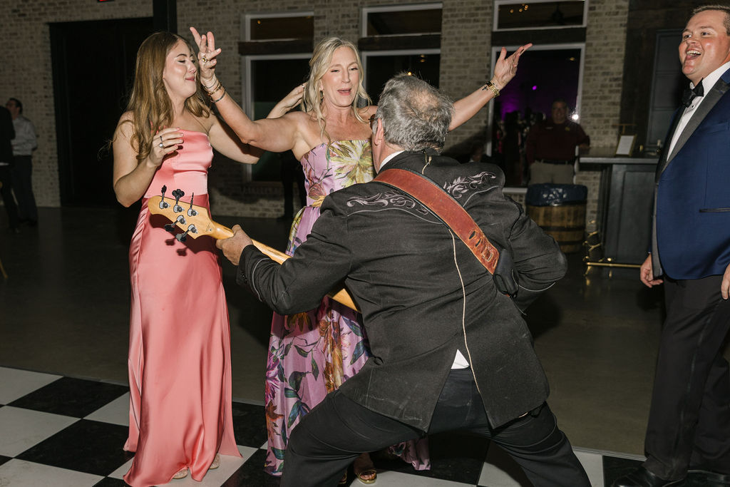 A member of the band plays guitar on the dance floor while the mother of the bride claps along, adding personality and fun to this vibrant Houston wedding reception.