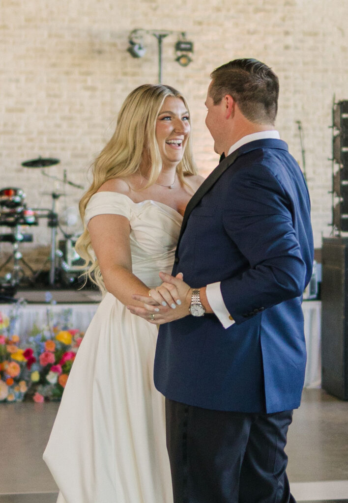 The bride and groom smile at each other mid-dance on the black-and-white reception floor, framed by live band equipment and florals.