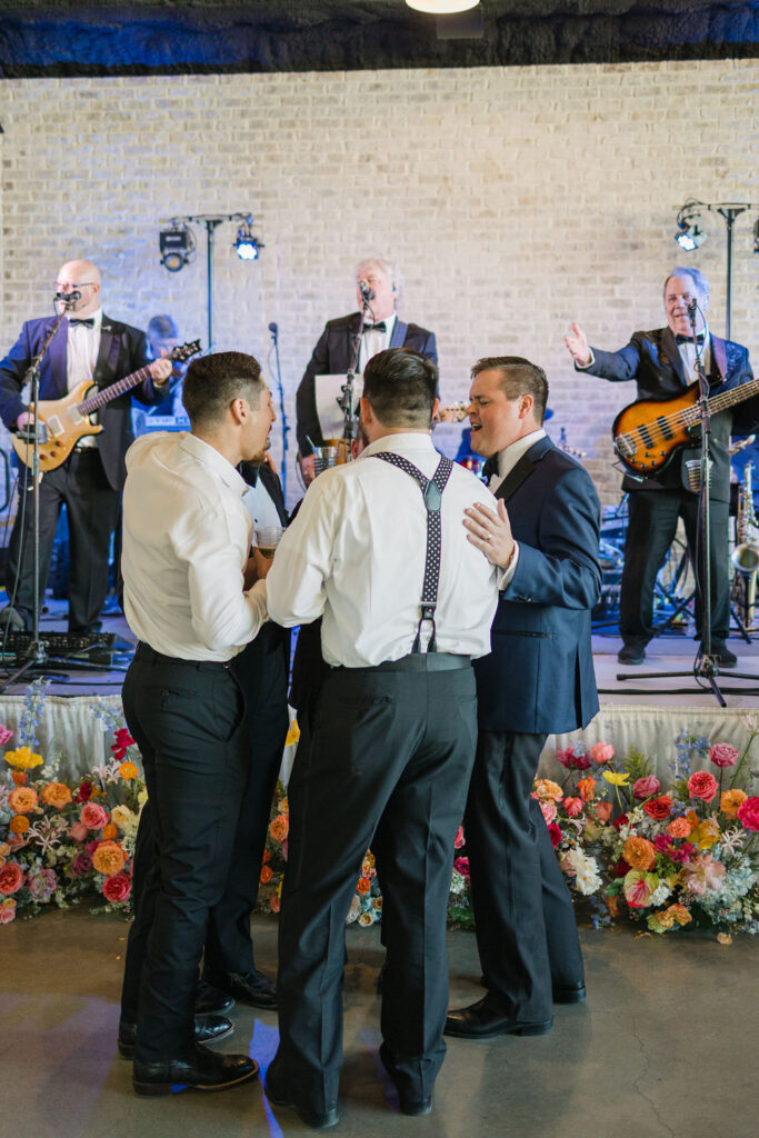 A live band performs at the wedding reception, framed by vibrant florals on the stage at this modern Texas wedding venue.