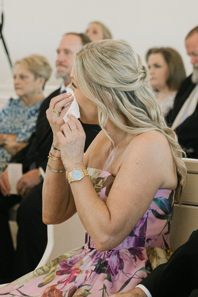 Mother of bride wipes away tears while seated in the chapel during the ceremony, overwhelmed with emotion at this meaningful celebration in Camp Hosea’s chapel.