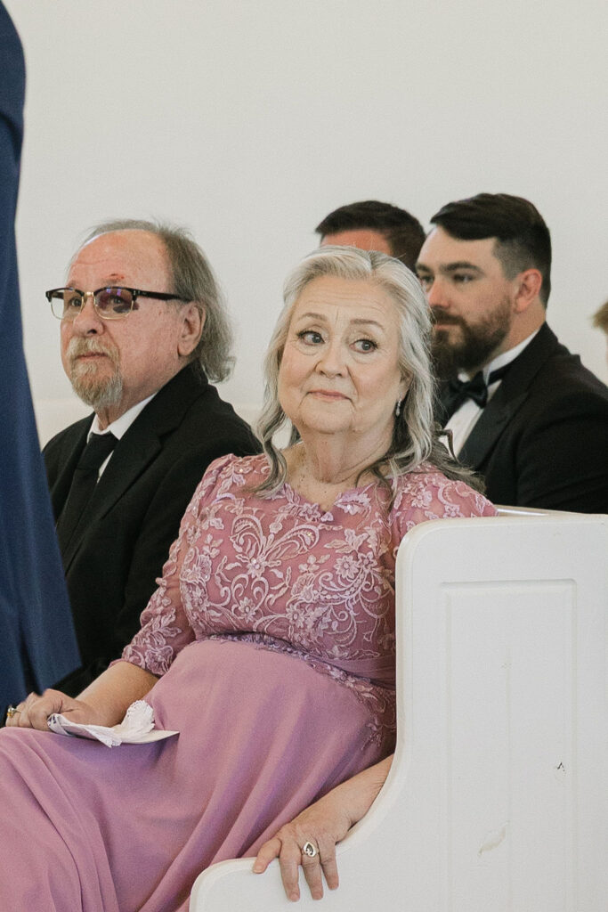 A mother of the groom sits near the front in a dusty lavender gown, proudly watching her son marry at this elegant Texas wedding.