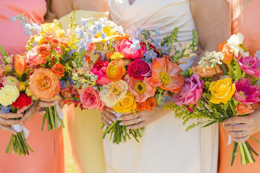 A close-up of the bride’s colorful bouquet with bold pinks, oranges, and yellows pops against her satin gown—perfect for couples seeking colorful wedding inspiration.