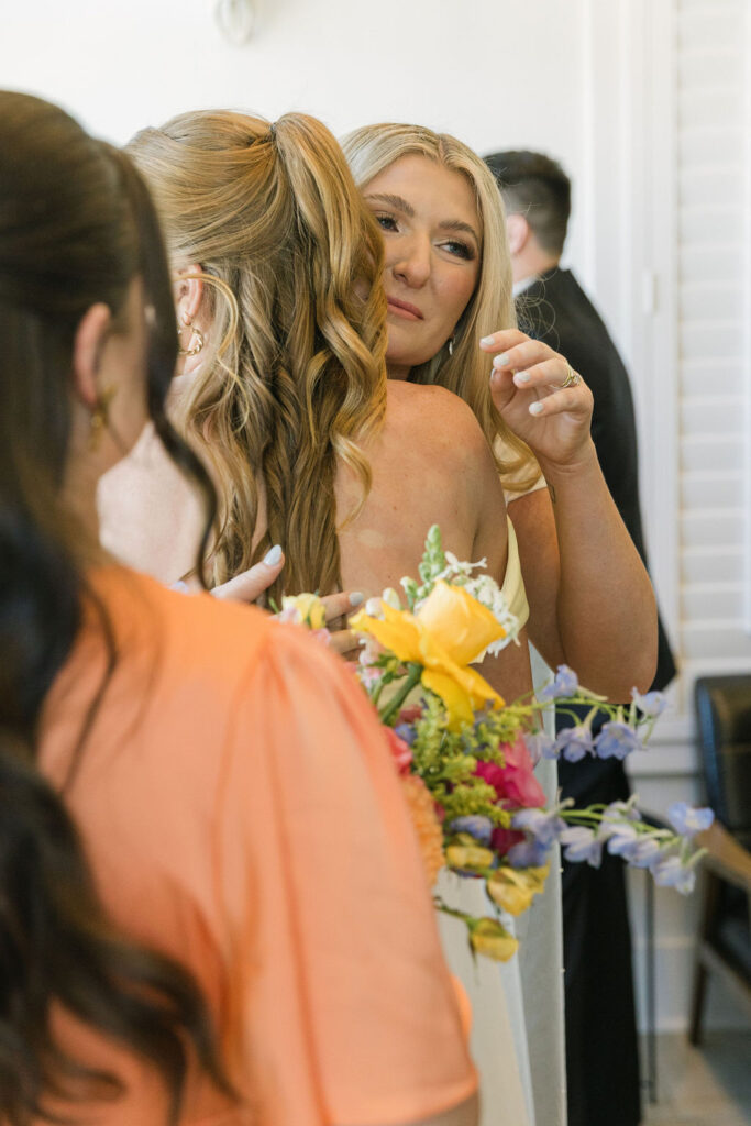 A candid hug between the bride and her sister holding a bouquet of yellow and lavender florals, showing warm connection and celebration.