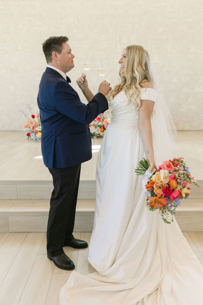 The couple toasts with champagne after the ceremony, celebrating with bright florals and soft light filling the Camp Hosea chapel.