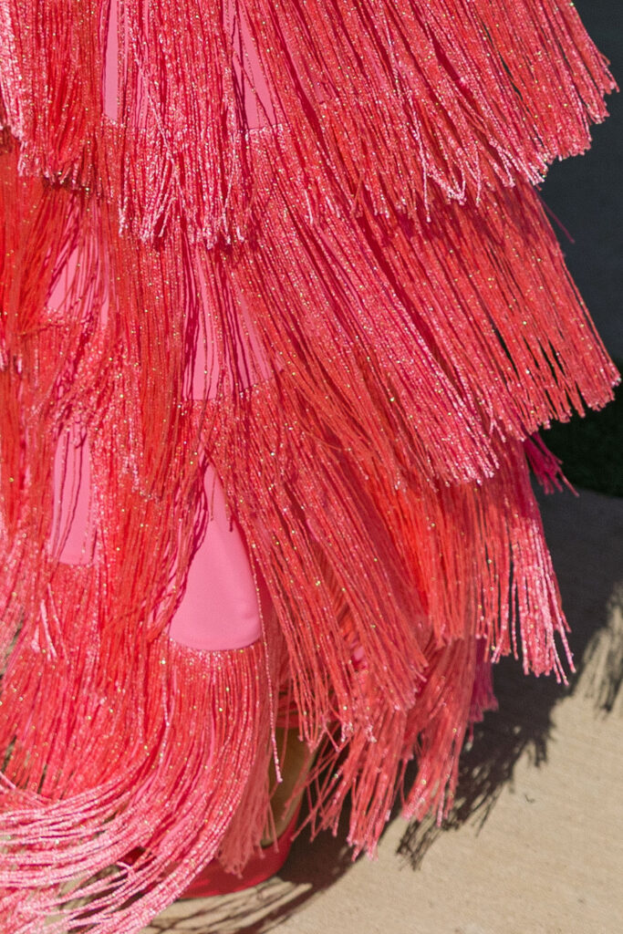 A vibrant pattern of pink fringe layers catches the light—showcasing festive, fashion-forward guest attire at this colorful Camp Hosea wedding.