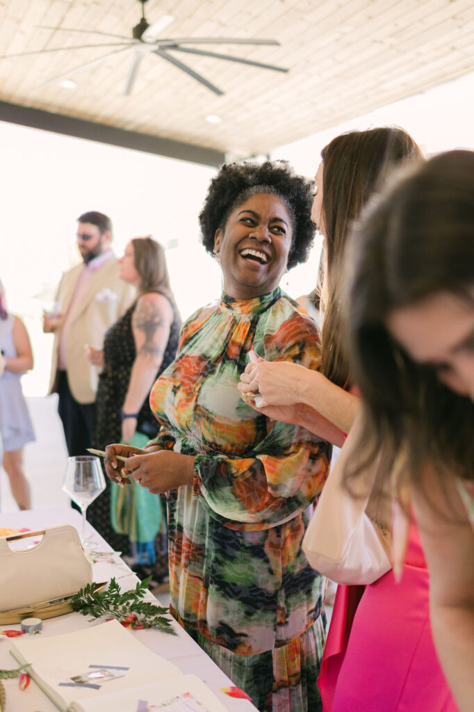 A smiling guest in a patterned floral dress chats during cocktail hour outside the modern reception hall of this Houston-area wedding.