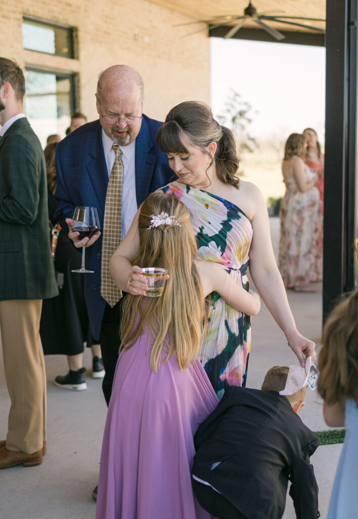 Candid of a mom hugging her daughter during cocktail hour, with spring florals and guests mingling in the background outside the modern venue.