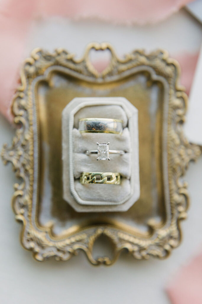 Wedding rings displayed in a velvet box on an ornate gold tray, styled with soft pink fabric—perfect for couples looking for elegant wedding detail inspiration in Texas.