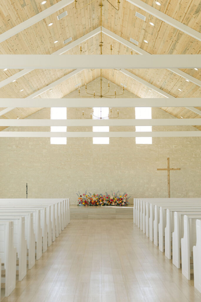 Wide view of Camp Hosea's beautiful modern white chapel adorned with a colorful ground floral arch.