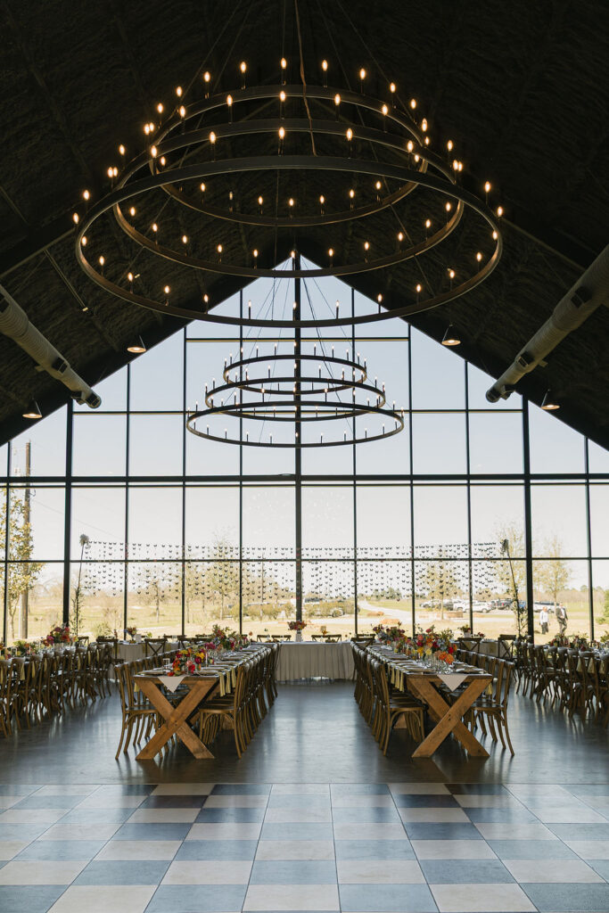 A wide view of Camp Hosea’s black-ceiling reception hall, glowing with warm chandeliers and set for a colorful and modern Texas wedding celebration.