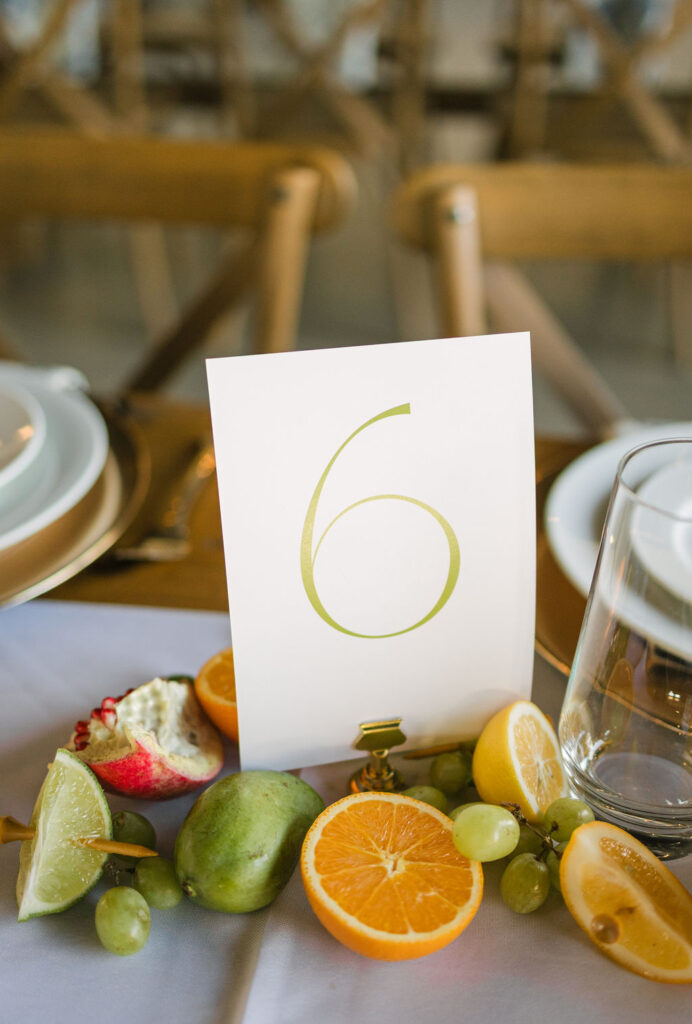 Simple modern table number placed in vibrant fruit at this colorful Camp Hosea wedding reception.