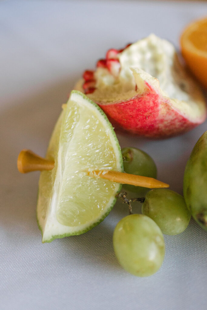 A close-up of fruit-inspired table decor includes sliced limes, grapes, and florals that create a fresh, colorful reception design at Camp Hosea.