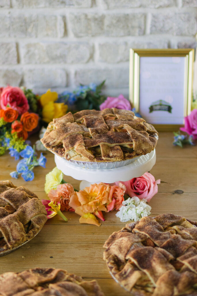 A rustic pie table decorated with bold spring florals replaces a traditional wedding cake, adding warmth and personality to this Texas wedding dessert display.