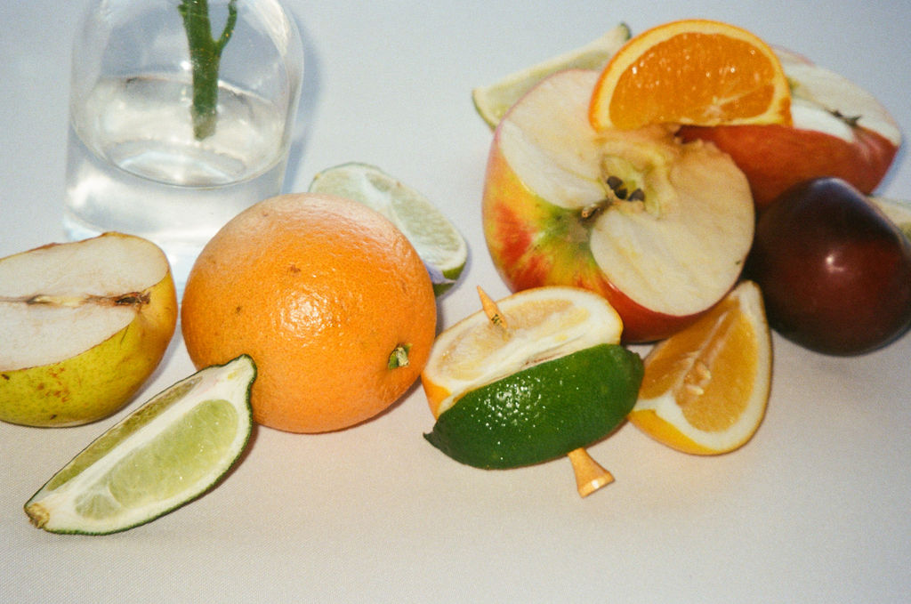 A close-up detail of fresh citrus fruit styled for reception decor, including oranges and green apples with golf tees—a playful nod to the couple’s personality.