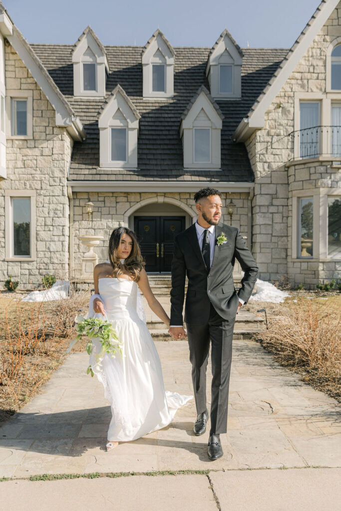 Bride and groom walk hand-in-hand outside Greystone Castle on their patio