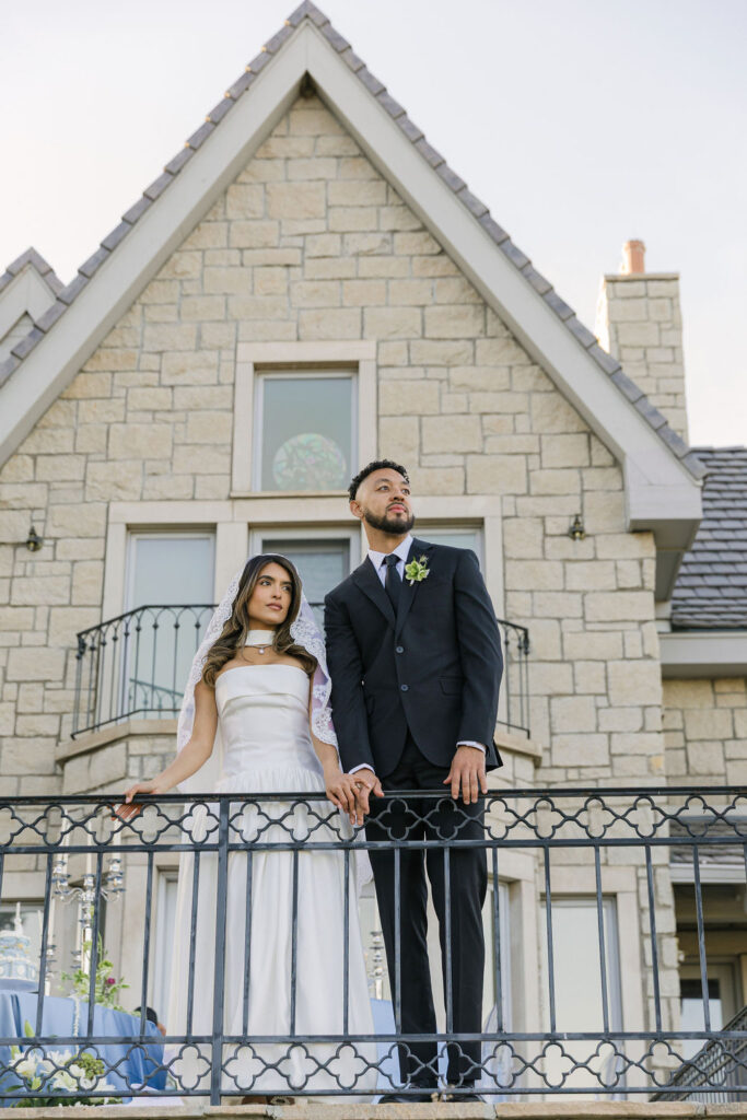 Bride and groom posing on the ornate balcony railing at Greystone Castle