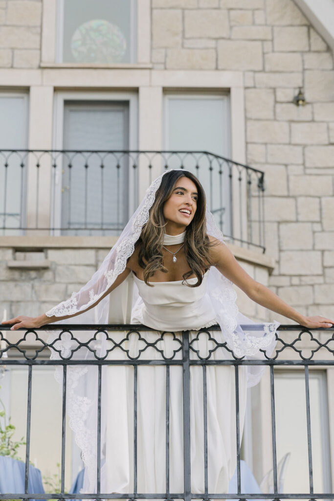 Bride smiles joyfully while leaning on the ornate balcony railing at Greystone Castle