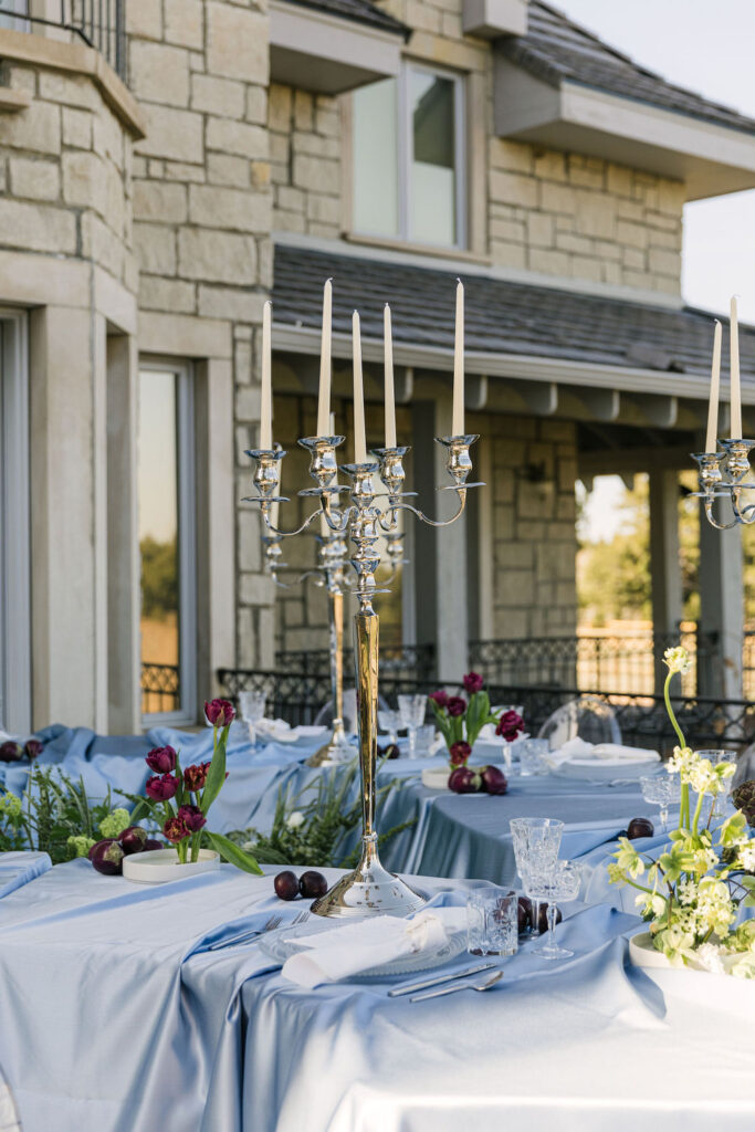 Outdoor wedding reception space set up at Greystone Castle adorned with elegant florals, and tall silver candelabras, all set against the elegant stone exterior.