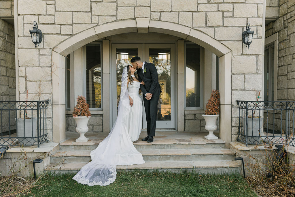Bride and groom kissing outside Greystone Castle, the stone exterior and dramatic architecture framing their joyful exit in golden afternoon light.