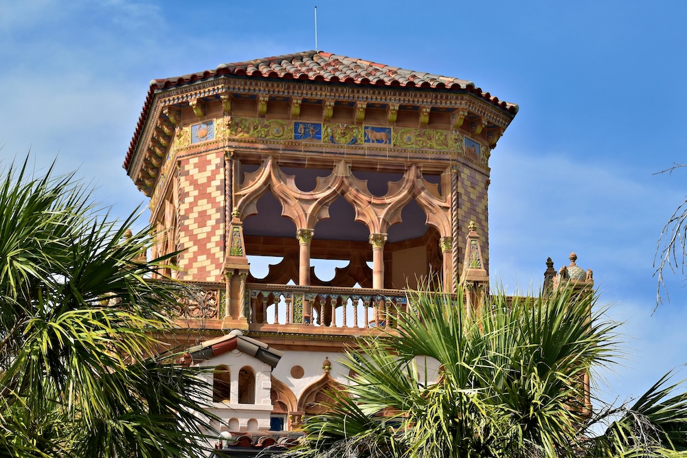 The upper turret of Ca’ d’Zan at The Ringling Museum peeking through palm trees under a blue sky, showcasing one of the most picturesque wedding venues in Florida.