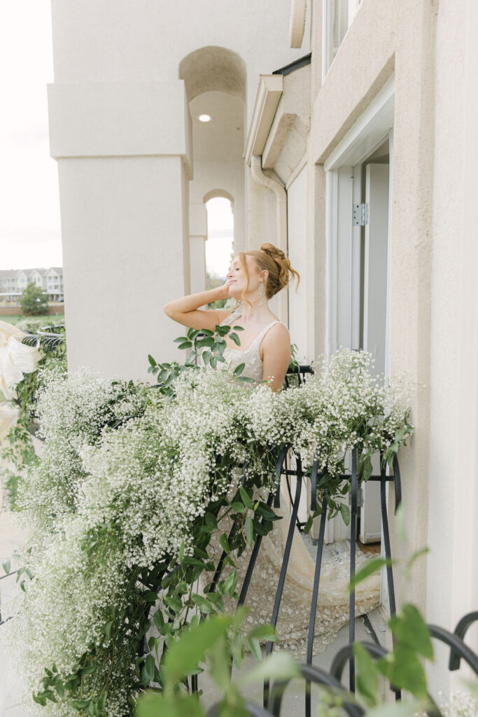 Bride enjoys a quiet moment on a balcony overflowing with baby’s breath and greenery at Chateaux at Fox Meadows