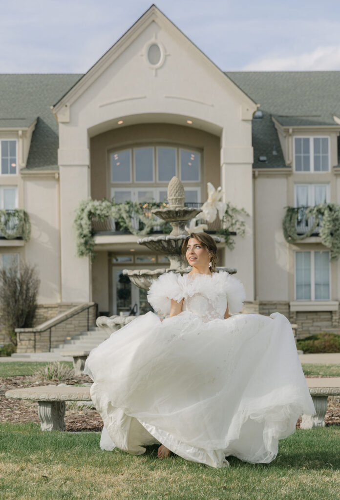 Bride twirls in a voluminous tulle wedding gown with dramatic ruffled sleeves, radiating joy in front of the grand entrance of Chateaux at Fox Meadows