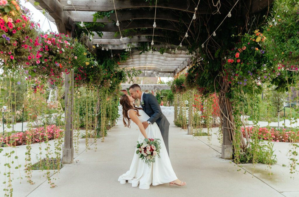 Bride and groom doing a dip and kiss underneath a colorful floral and lush green arched walkway at a Colorado garden wedding venue