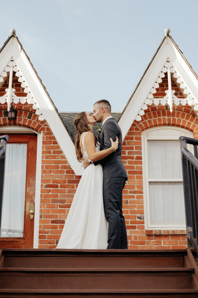 Bride and groom kissing at the top of the stairs in front of the quaint cabins at a garden wedding venue