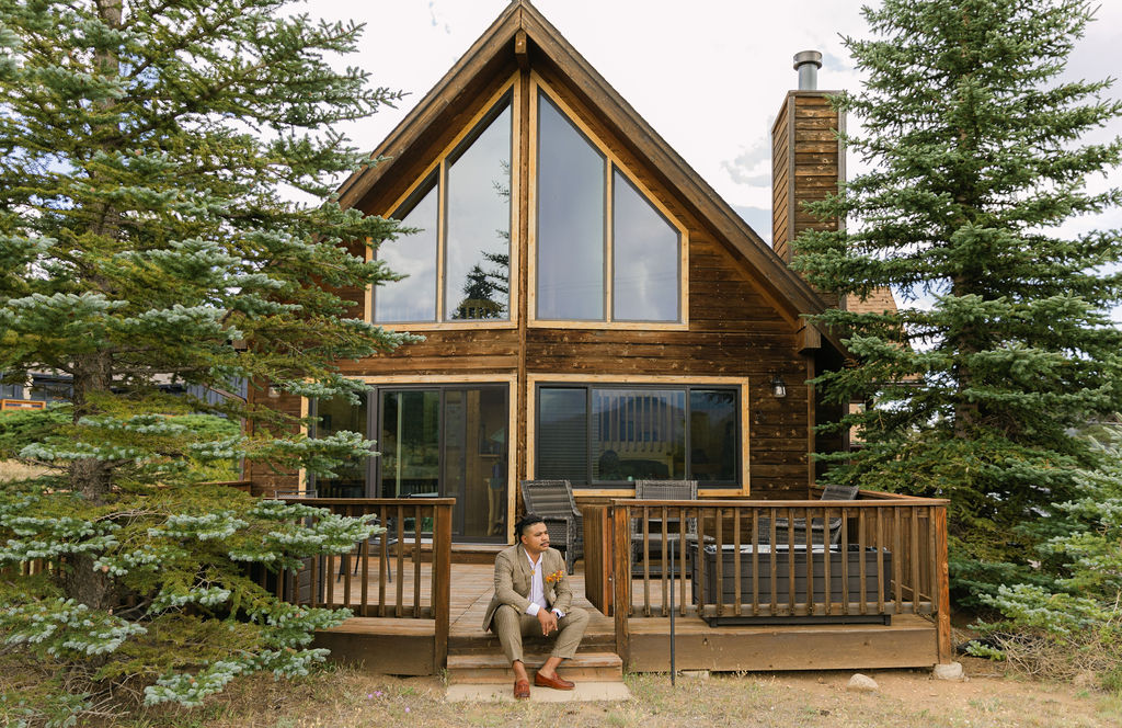 groom sitting in front of the wooden lodge