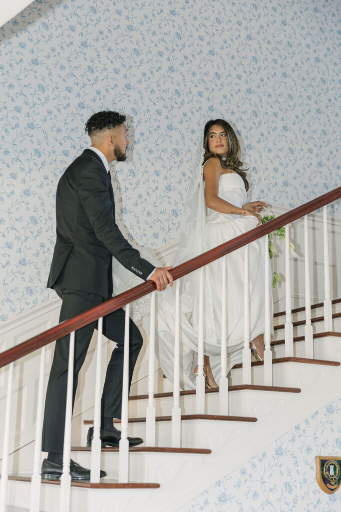 bride and groom walking up the stairs with cute vintage wallpaper in the background