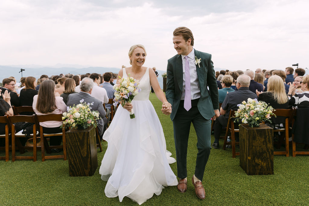 Joyful bride and groom holding hands exiting their luxury mountain wedding ceremony in Colorado 