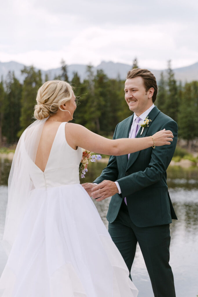 Joyful first look in the mountains by a lake between a bride and groom 