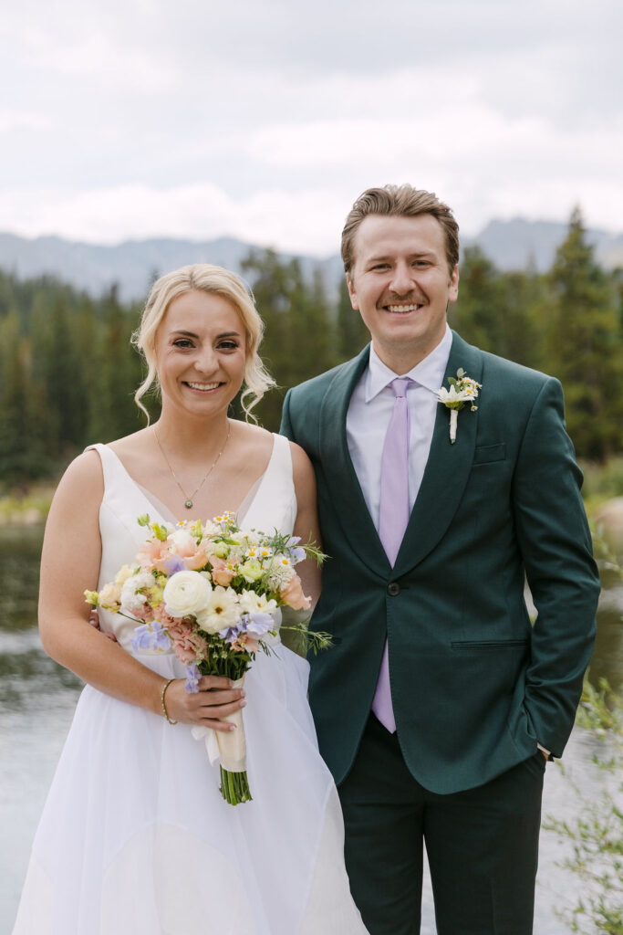 Classic portrait of a bride and groom smiling in the mountains with colorful florals 
