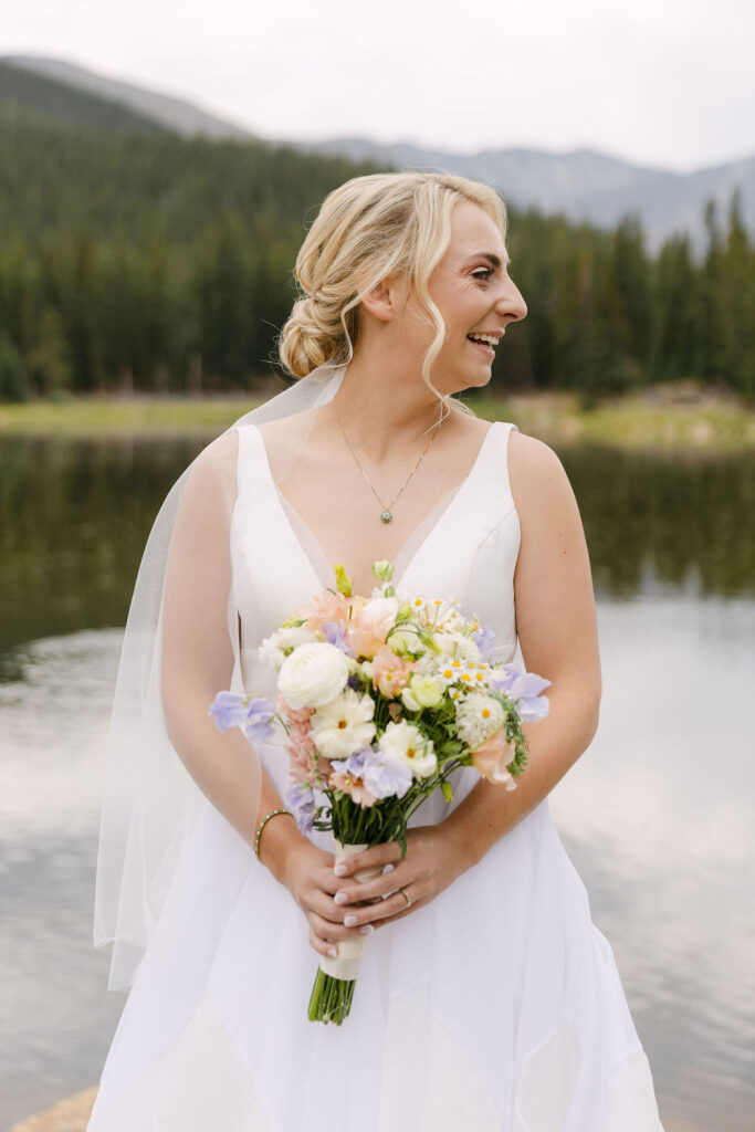 Joyous bride laughing in the mountains and holding a colorful pastel floral bouquet